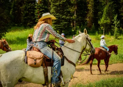 A group of horseback riders in yellowstone park. A lady close to the camera riding a white horse with a lush green background